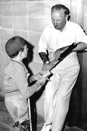 Legendary Australian cricketer Don Bradman signing a bat for a boy crippled by polio and wearing calipers.