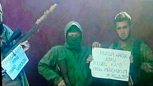 Members of the Syria-based jihadist group Jabhat Fatah al-Sham hold a sign that reads "Punish Ahok or our bullets will".
