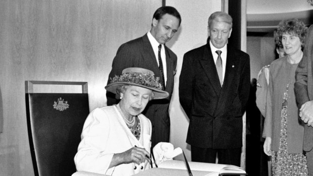 The Queen signs the visitors' book at Parliament House, while prime minister Paul Keating and Parliament House officials look on in February 1992. 