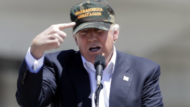 Donald Trump gestures to his camouflaged "Make America Great" hat at a campaign rally.