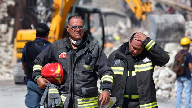 An emergency services worker puts his hand on his head as he walks from rubble in Amatrice.