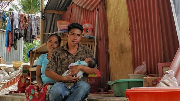 Hanan holds baby Akila, his wife Reniatun behind him, in their makeshift home.