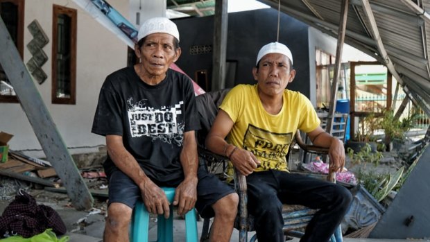 Tamrin, left, with his son Bobi in front of his damaged house.