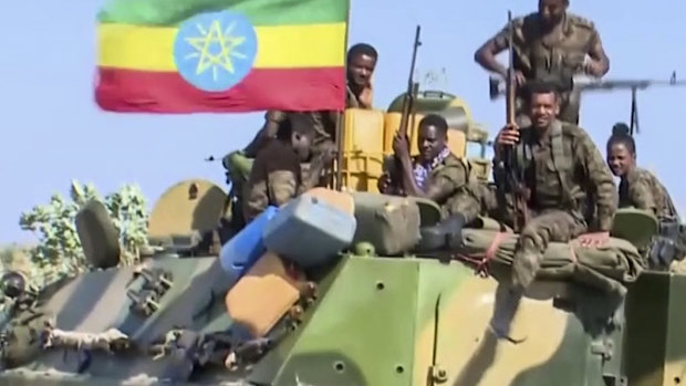 Ethiopian military sitting on an armored personnel carrier next to a national flag, on a road in an area near the border of the Tigray and Amhara regions of Ethiopia.