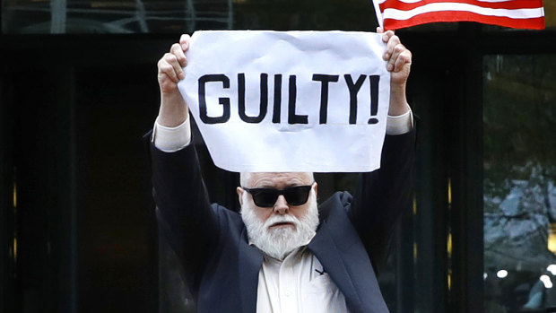Protester Bill Christeson holds up a sign as the first count of guilty comes in.