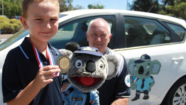 Evatt Primary School student Aaron Zorzi, who received a bravery medal for helping save his mother's life, with Constable Kenny Koala and Stewart Waters.