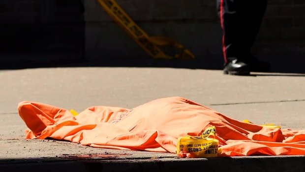 A police officer stands over a covered body in Toronto after a van mounted a sidewalk crashing into pedestrians on Monday, April 23, 2018. (Nathan Denette/The Canadian Press via AP)