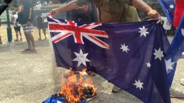 A protester holds the Australian flag over a fire.