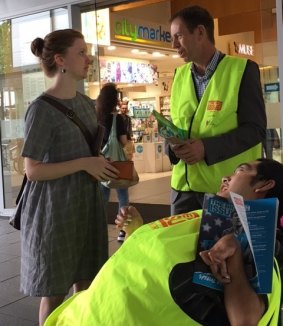 Greens MLA Shane Rattenbury sells The Big Issue with vendor Tau while speaking to a prospective customer.