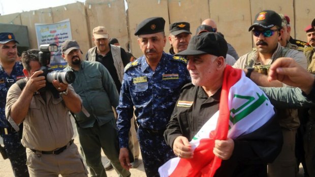 Iraq's Prime Minister Haider al-Abadi holds a national flag upon his arrival in Mosul.