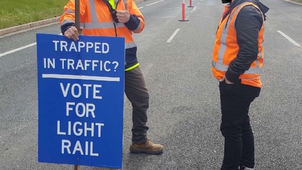 Road workers hold pro-light rail signs in Woden.
