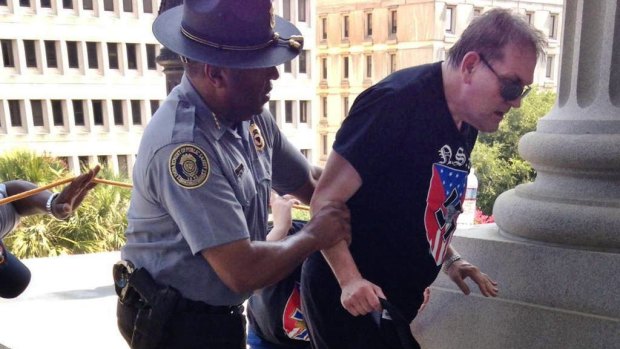 Police officer Leroy Smith, left, helps a man wearing National Socialist Movement attire up the stairs during a rally in Columbia, on July 18.