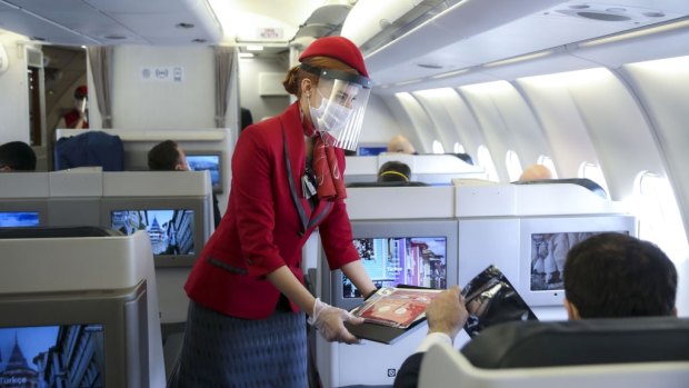 A stewardess wearing a face shield serves business class travellers.