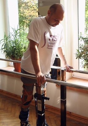 Darek Fidyka walks with the assistance of parallel bars and leg braces.