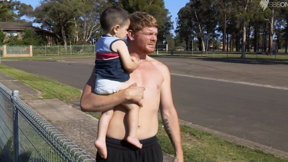Corey holds his two-year-old son in season one of <i>Struggle Street</i>.