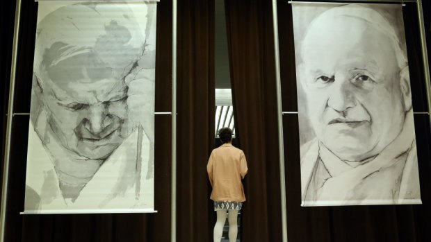 A woman enters a courtain between the images of Pope John Paul II and Pope John XXIII as Archbishop of Krakow and former personal secretary of the late Pope John Paul II.