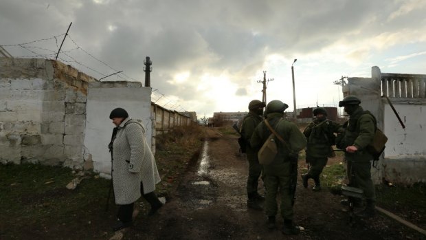 Gloom: A woman passes unidentified Russian soldiers at the Ukrainian base in Perevalnoye.