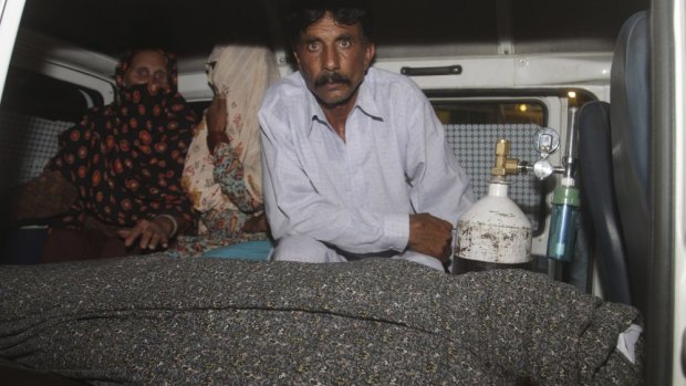 Grieving husband: Mohammad Iqbal, right, sits in an ambulance next to the body of his pregnant wife, Farzana Parveen.