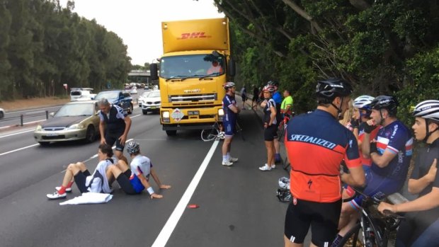 Michael Long (left) sits on the ground, propped up by another rider, before an ambulance arrives.