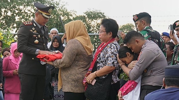 Brigadier Firman's widow receives the Indonesian flag from her husband's coffin as his younger brother Riswan, also an officer, consoles Firman's six-year-old daughter.