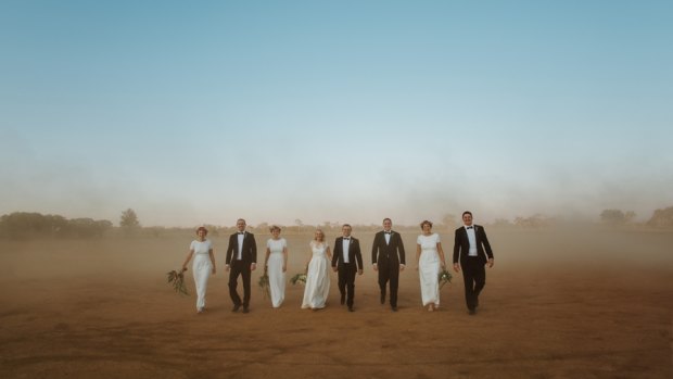 Ross Uebergang and Ingrid Wood walk with their wedding party across a dusty claypan cricket pitch at Blackall,