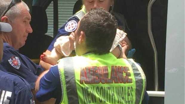 Emergency workers take a baby after a woman became trapped under a car in Newcastle on Friday. 