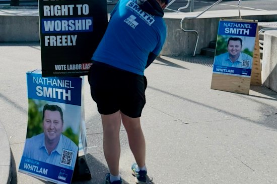 A man in a Liberal T-shirt putting up a poster authorised by Freedom Party candidate Morgan C. Jonas in the seat of Whitlam, NSW.