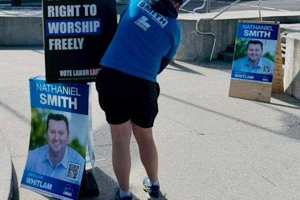 A man in a Liberal T-shirt putting up a poster authorised by Freedom Party candidate Morgan C. Jonas in the seat of Whitlam, NSW.