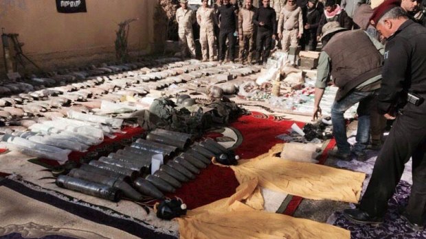 The Iraqi military displays confiscated Islamic State weapons and ammunition, with an IS flag placed upside down in the background as a mark of disrespect.