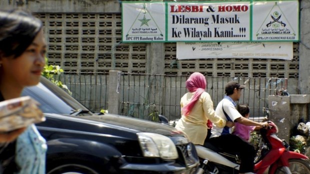 People negotiate the traffic past a banner put up by the hardline Islamic Defenders Front calling for gay people to leave the Cigondewah Kaler area in Bandung, West Java, Indonesia.
