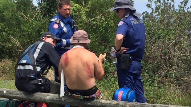 A man with a suspected broken collarbone speaks to paramedics after being washed off the rocks.