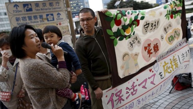 Makiko Morohoshi, holding her two-year-old son Amane, speaks next to her husband Kazuhiko at a rally in Tokyo in support of mothers and fathers whose children failed to secure places in daycare.
