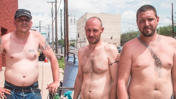 Three metal scrappers with a grocery cart along East Third Street pose for a moment on their way to the scrapyard.