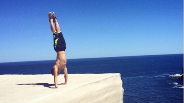 A man performs a handstand near the edge of Wedding Cake Rock.