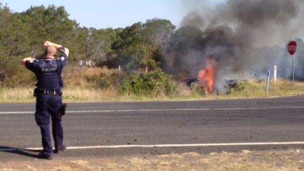 A police car burns after catching fire in grass beside a road west of Brisbane.