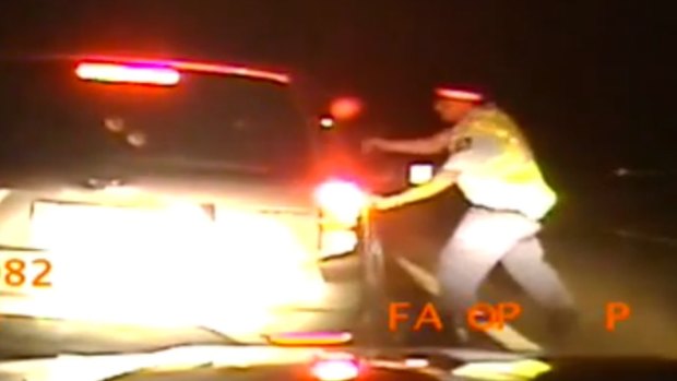 Police dash camera vision shows the officer running to the driver's side window with his gun drawn.