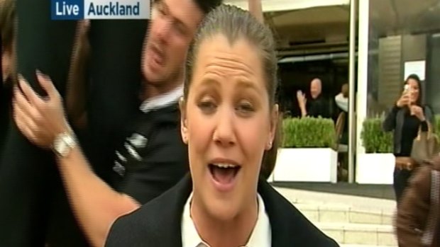 An All Blacks fan is lifted up in the air behind an ABC reporter.