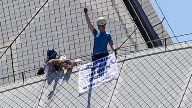 A protester raises his arm after being stopped by police from putting a protest sign on top of the Sydney Opera House