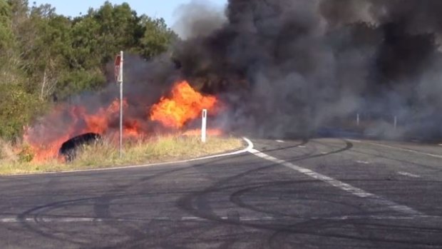 A police car burns after catching fire in grass beside a road west of Brisbane.