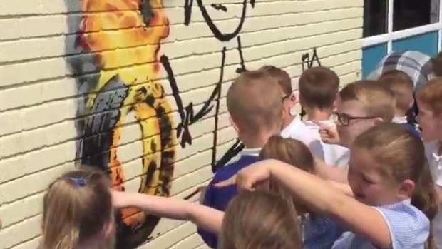 Children crowd around Banksy's mural after coming back from school holidays to their Bristol primary school.