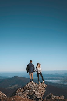 Van life influencers Harry and Jordan posing on a rock edge, with mountains in the background