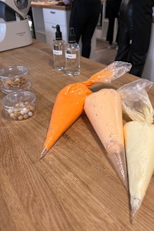 Three different levels of orange buttercream icing sit in piping bags waiting to make the ombre finish of the cake