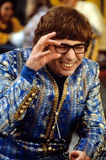 Mike Myers wearing an ornate blue jacket while squinting through his black rimmed glasses in a scene from the film 'Austin Powers: The Spy Who Shagged Me', 1999.