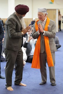 King Charles III makes the namaste gesture as a traditional shawl for meditation is placed around his shoulders in the Prayer Hall during a visit to the newly built Guru Nanak Gurdwara on December 06, 2022 in Luton, England 
