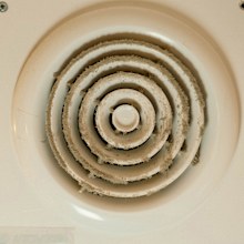 Close-up of a dirty electric duct fan and blades inside a bathroom extractor hood, showing the need for cleaning to ensure proper ventilation and maintain air quality in the bathroom environment.