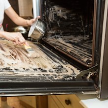 Person applying mixed baking soda onto surface of oven for effective and safe cleaning
