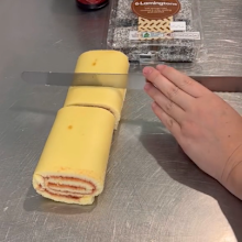 Woman slicing vanilla scrolls with jam inside in preparation for a Christmas "wreath" dessert.