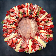 Birds eye view shot of "Scramington wreath" dessert that consists of home-made whipped cream between vanilla and jam scrolls, and lamingtons, sitting on a wooden plate.