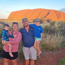 Mum, dad and two kid pose in front of Uluru at sunset