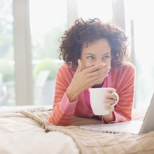 Woman covering her smile and holding a coffee mug